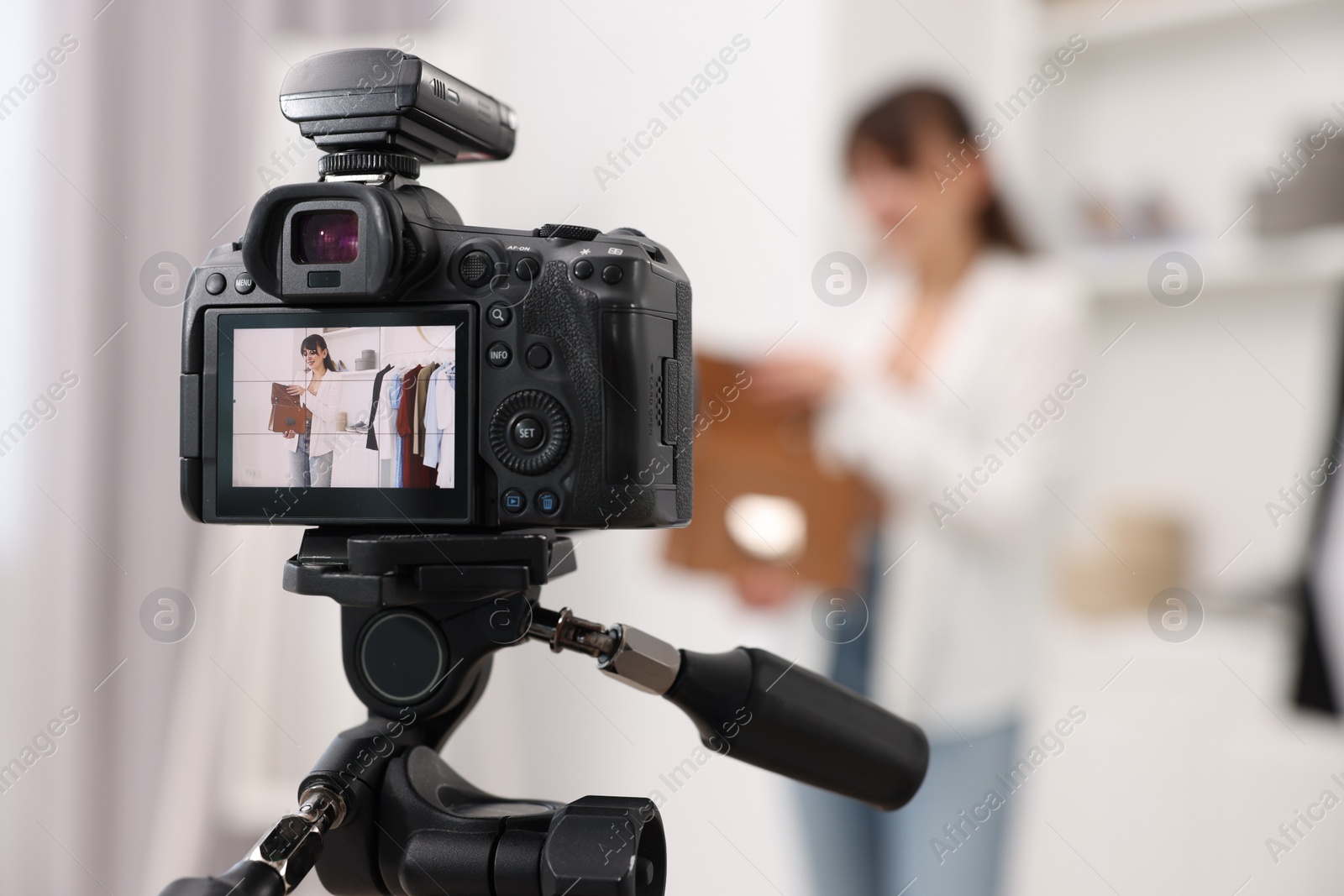 Photo of Fashion blogger showing her clothes while recording video at home, focus on camera