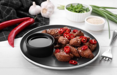 Photo of Plate with tasty soy sauce and roasted meat served on white wooden table
