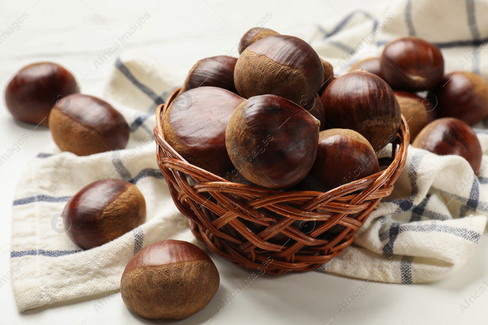 Photo of Sweet fresh edible chestnuts in wicker bowl on white table, closeup