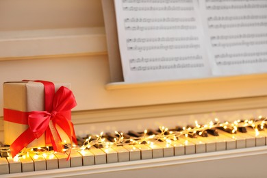 Photo of Gift box and fairy lights on piano keys, closeup. Christmas music