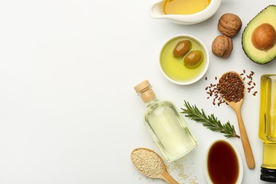 Photo of Vegetable fats. Different oils in glass bottles and ingredients on white table, flat lay. Space for text