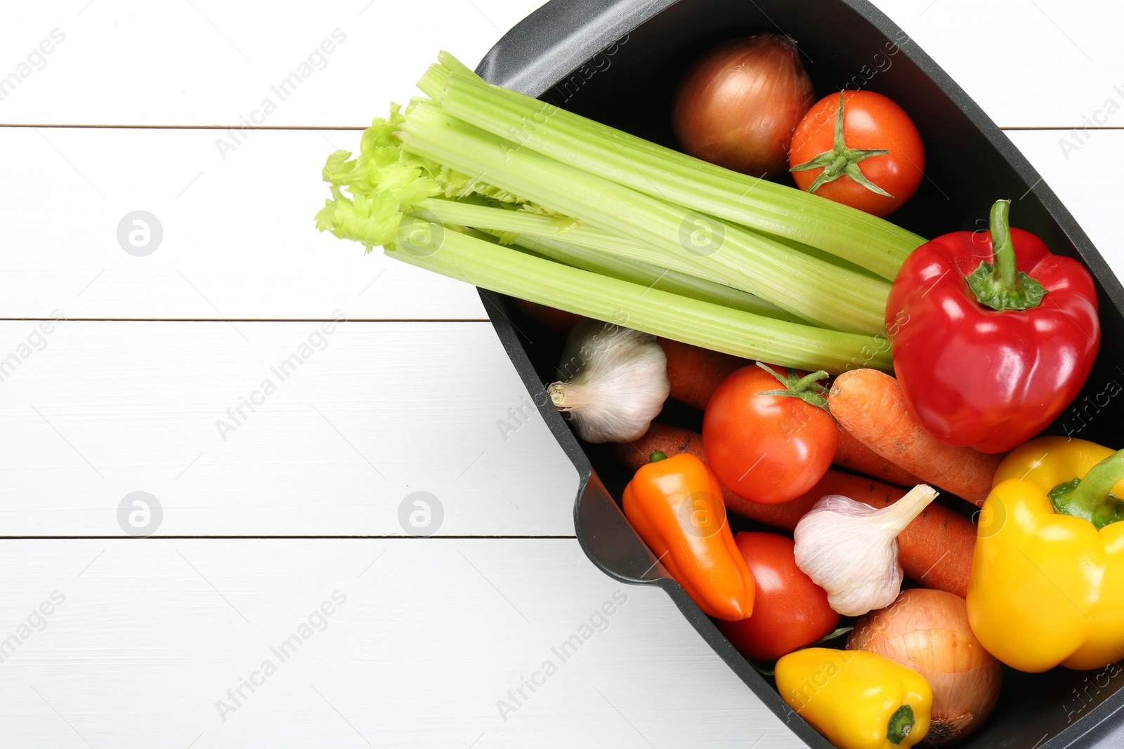 Photo of Black pot with fresh vegetables on white wooden table, top view. Space for text