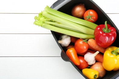 Photo of Black pot with fresh vegetables on white wooden table, top view. Space for text