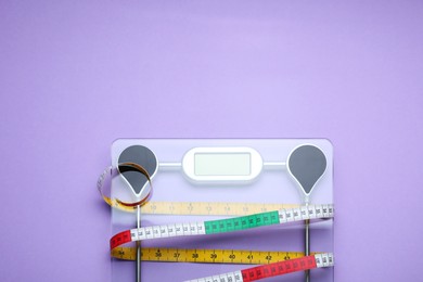 Electronic scales and measuring tape on violet background, top view. Space for text