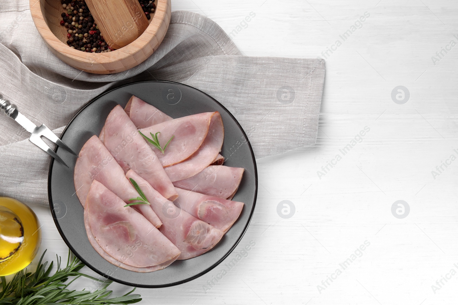 Photo of Tasty ham with rosemary and carving fork on white wooden table, flat lay. Space for text