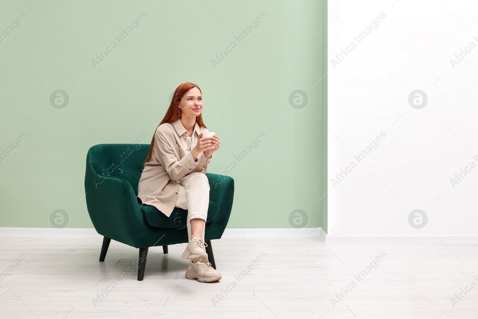 Photo of Beautiful young woman with cup of drink sitting in armchair indoors. Space for text