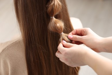 Photo of Professional stylist braiding woman's hair on blurred background, closeup