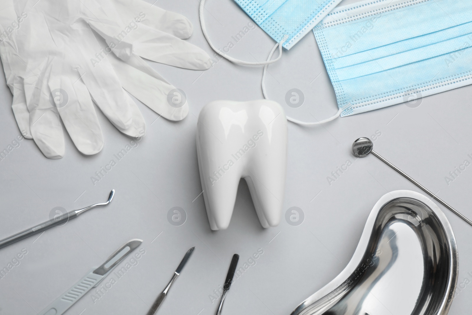 Photo of Tooth shaped holder, set of different dentist's tools, face masks and gloves on light grey background, flat lay