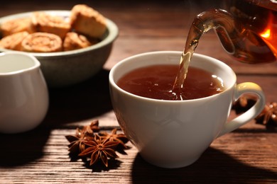 Photo of Pouring aromatic anise tea into cup on wooden table
