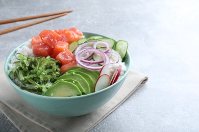 Photo of Delicious poke bowl with salmon, seaweed and vegetables served on light grey table. Space for text