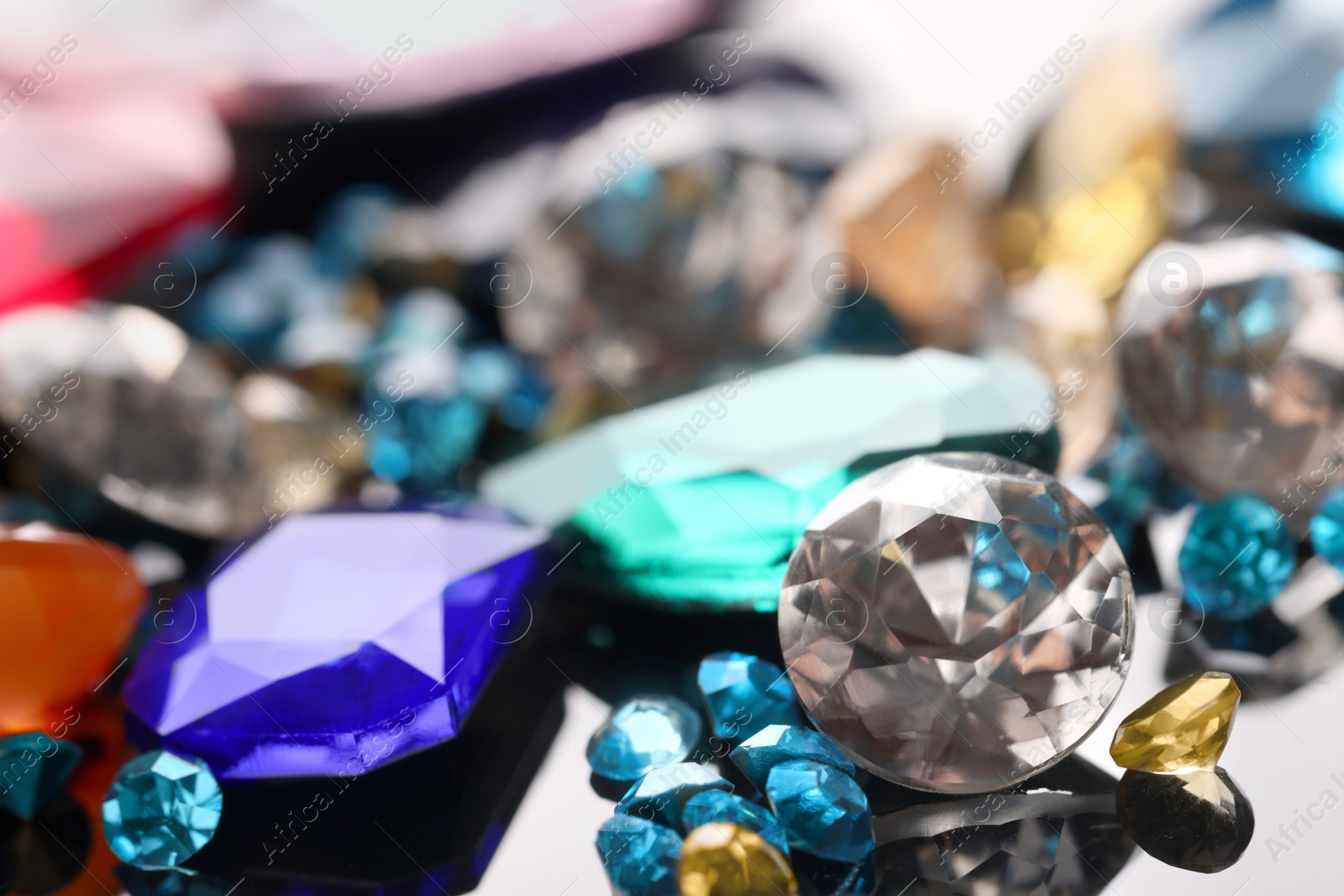 Photo of Different beautiful gemstones for jewelry on mirror surface, closeup