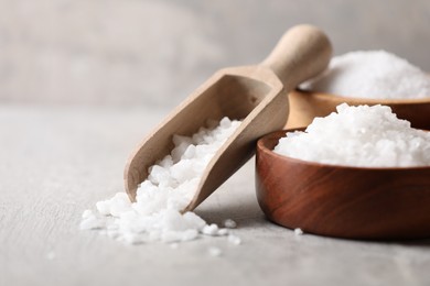 Photo of Natural salt in bowls and scoop on grey table, closeup