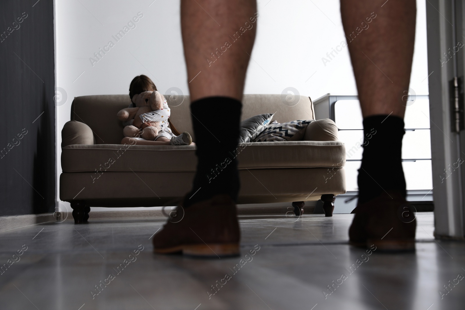 Photo of Adult man without pants standing in front of scared little girl indoors. Child in danger