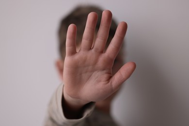 Photo of Child abuse. Boy doing stop gesture on light grey background, selective focus