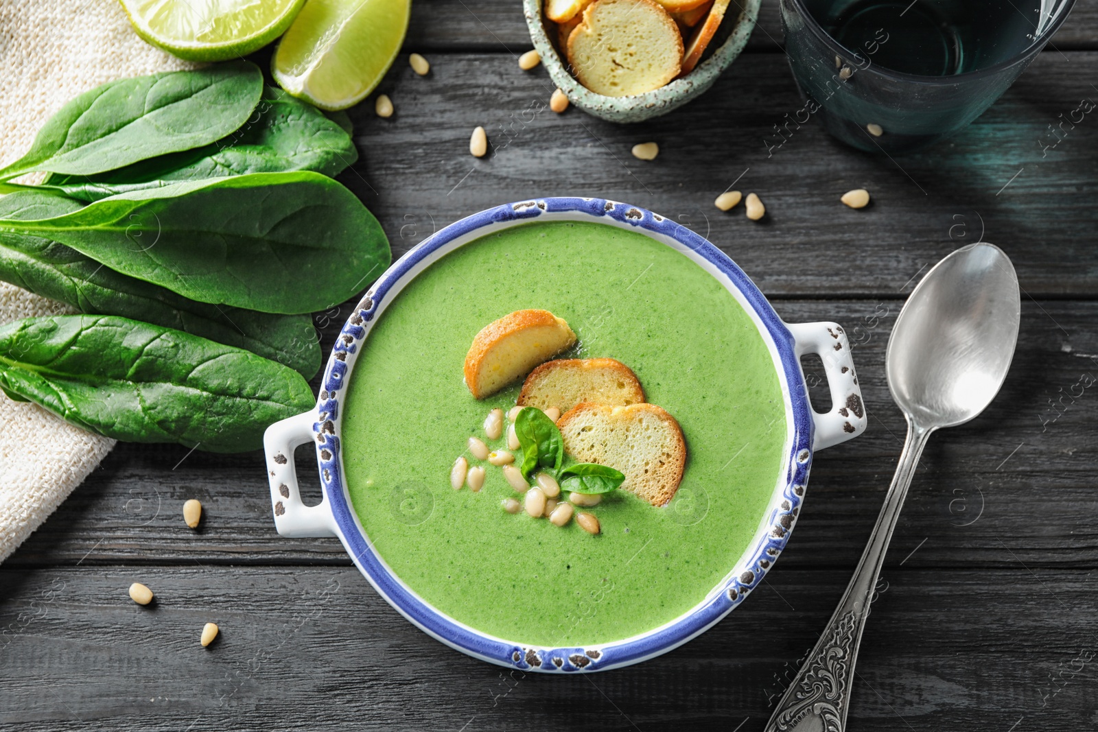 Photo of Bowl of healthy green soup with fresh spinach on grey wooden table, flat lay