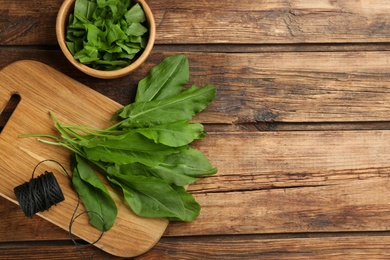 Photo of Fresh green sorrel leaves and thread on wooden table, flat lay. Space for text