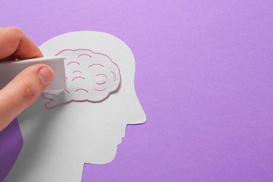 Photo of Woman erasing brain on human head paper cutout on violet background, top view with space for text. Dementia concept