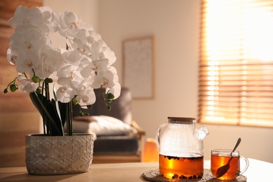 Photo of Beautiful orchid, teapot and cup with hot tea on table indoors