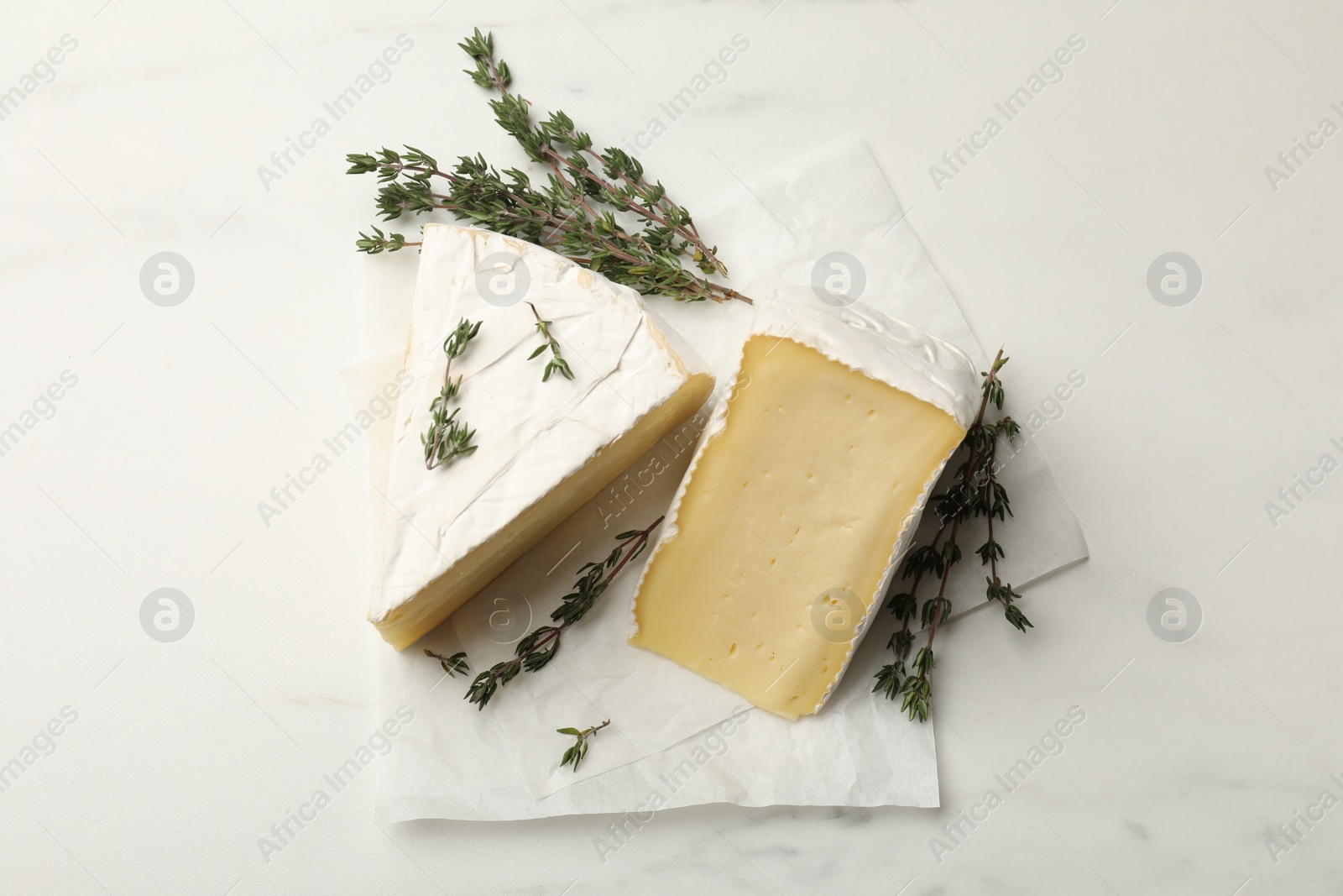 Photo of Pieces of tasty camembert cheese and thyme on white table, top view