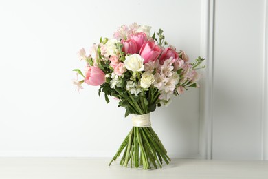 Photo of Beautiful bouquet of fresh flowers on table near white wall