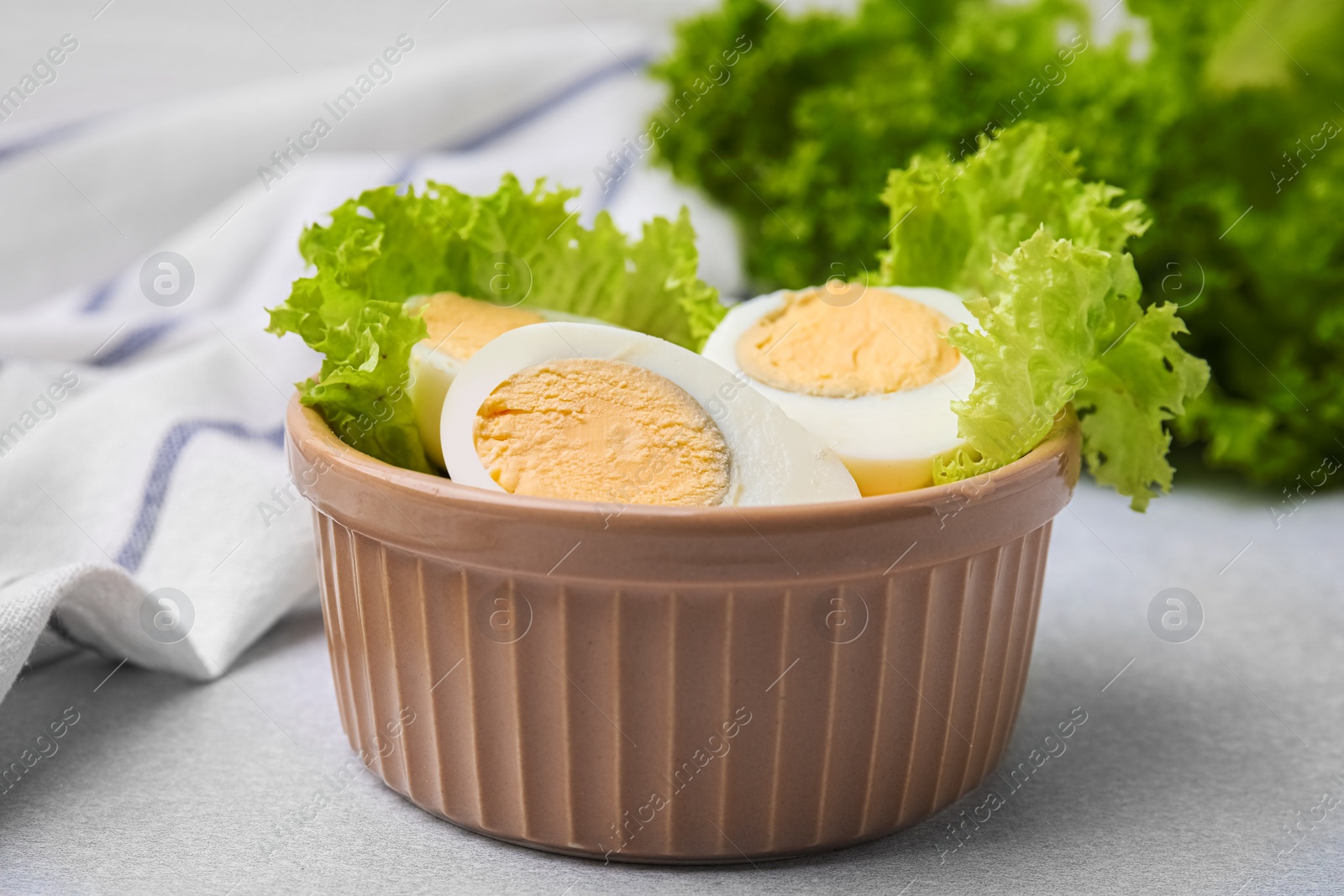 Photo of Fresh hard boiled eggs and lettuce on light grey table, closeup
