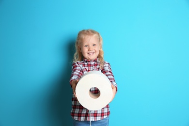 Cute little girl holding toilet paper roll on color background