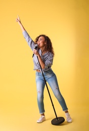 Curly African-American woman singing in microphone on color background