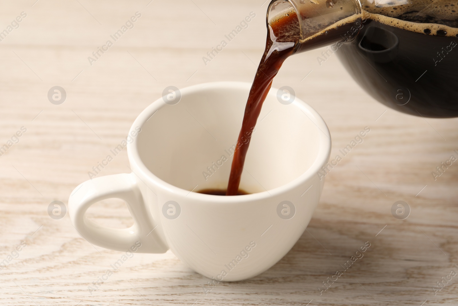 Photo of Pouring coffee into cup at light wooden table, closeup