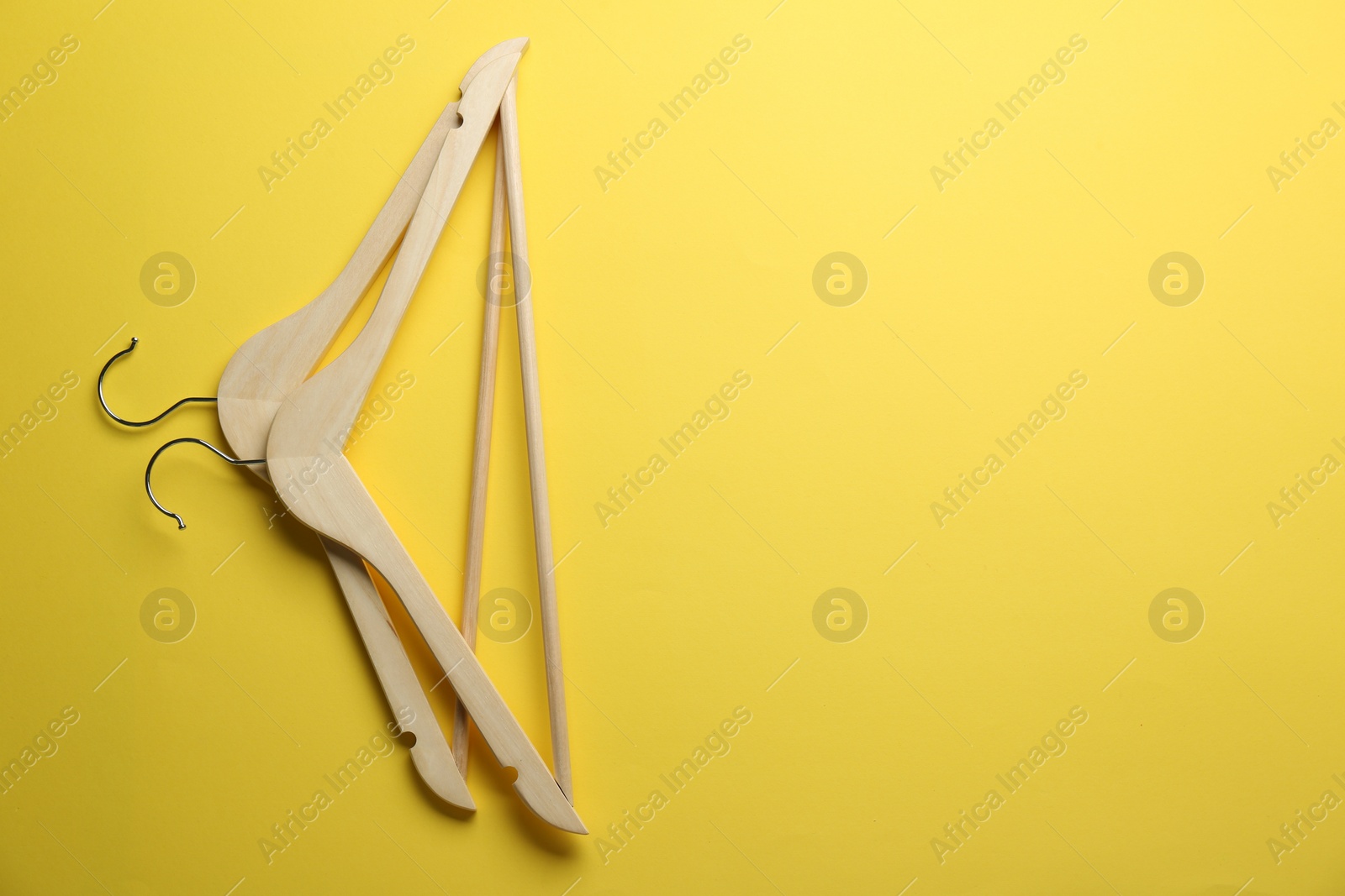 Photo of Wooden hangers on yellow background, top view. Space for text