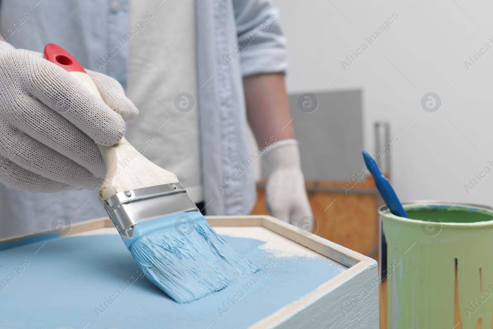 Photo of Man painting honeycomb shaped shelf with brush indoors, closeup. Space for text