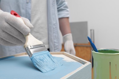 Photo of Man painting honeycomb shaped shelf with brush indoors, closeup. Space for text