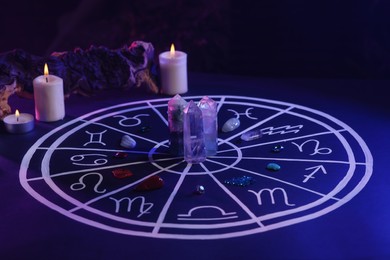 Natural stones for zodiac signs, drawn astrology chart and burning candles on dark blue table. Color tone effect