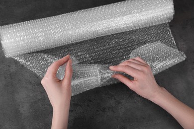 Photo of Woman covering wineglass with bubble wrap at dark grey table, closeup