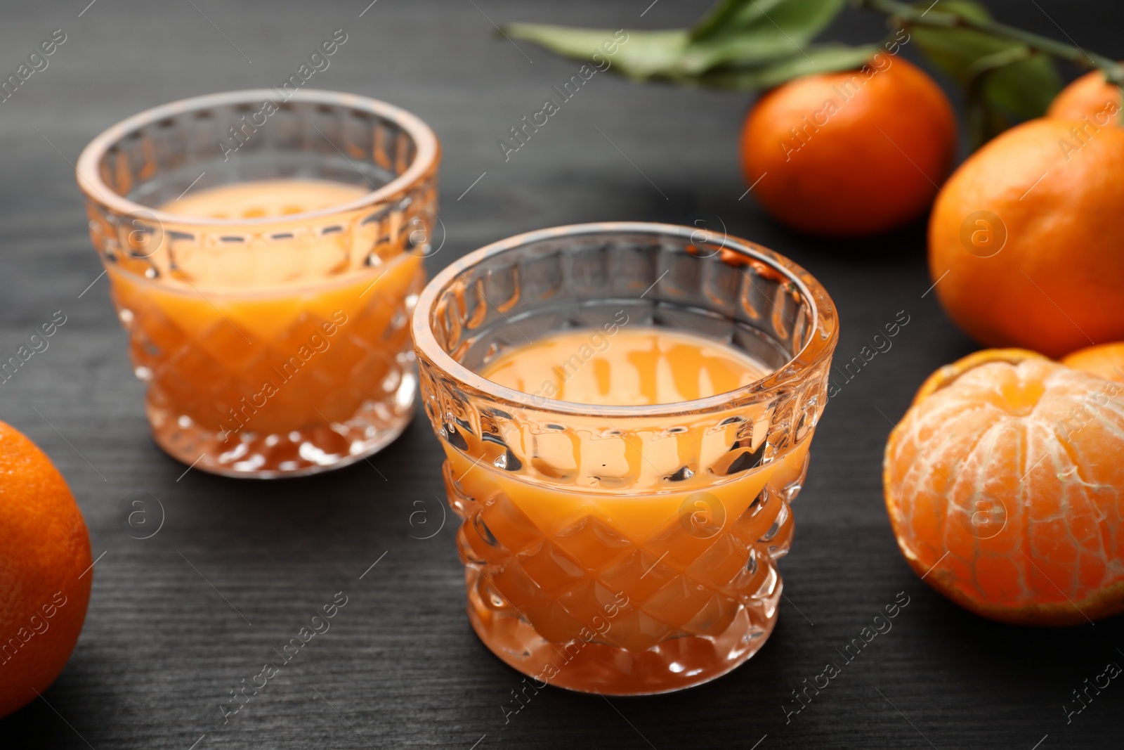 Photo of Tasty tangerine liqueur in glasses and fresh fruits on black wooden table