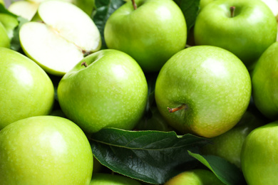 Photo of Pile of tasty green apples with leaves as background, closeup