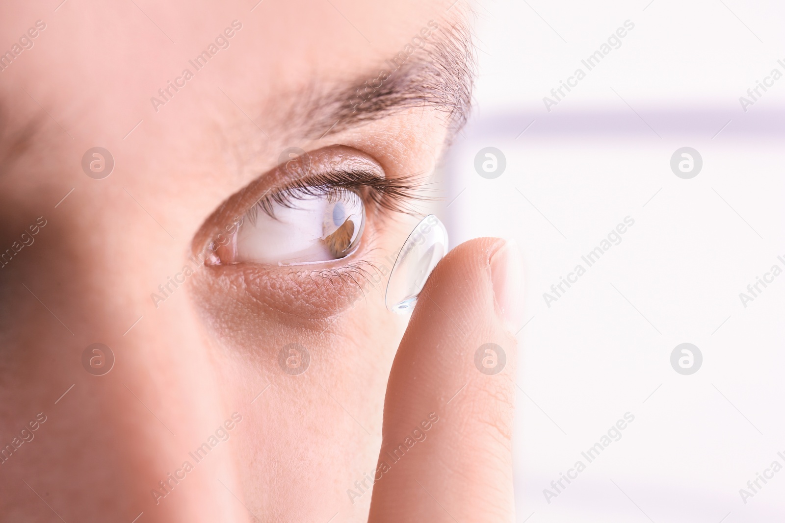 Photo of Young man putting contact lens in his eye, closeup