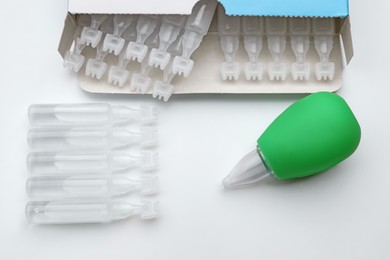 Photo of Single dose ampoules of sterile isotonic sea water solution and nasal aspirator on white background, top view
