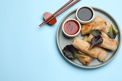 Photo of Tasty fried spring rolls, lettuce and sauces served on light blue table, top view. Space for text