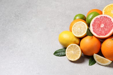 Photo of Pile of different fresh citrus fruits and leaves on grey textured table, closeup. Space for text