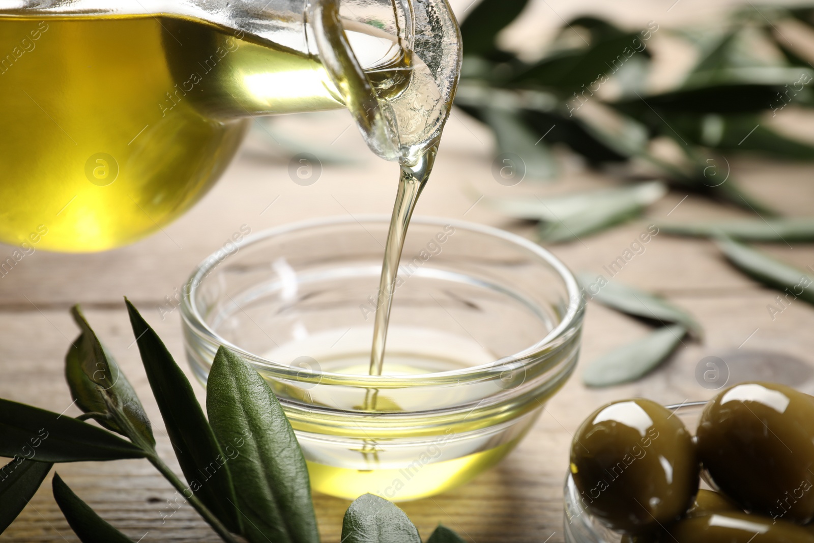 Photo of Pouring olive oil from jug into bowl on wooden table, closeup. Healthy cooking