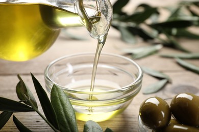Photo of Pouring olive oil from jug into bowl on wooden table, closeup. Healthy cooking