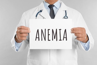 Image of Doctor holding sign with word ANEMIA on light grey background, closeup