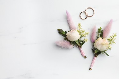 Photo of Small stylish boutonnieres and rings on white marble table, flat lay. Space for text