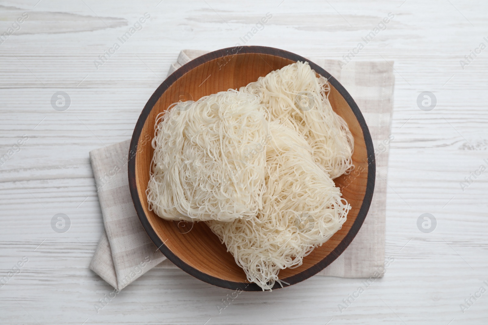 Photo of Bowl with dried rice noodles and napkin on white wooden table, top view