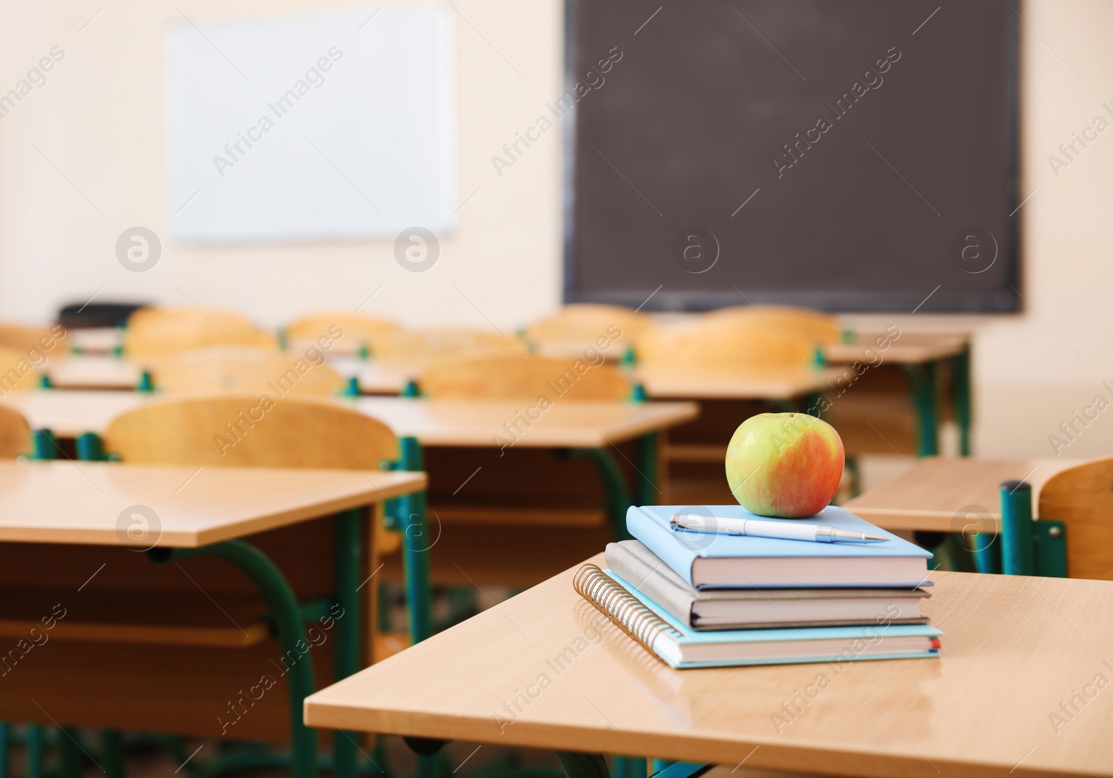 Photo of Stack of books and apple on desk in classroom