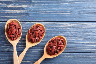 Dried goji berries in spoons on blue wooden table, flat lay. Space for text