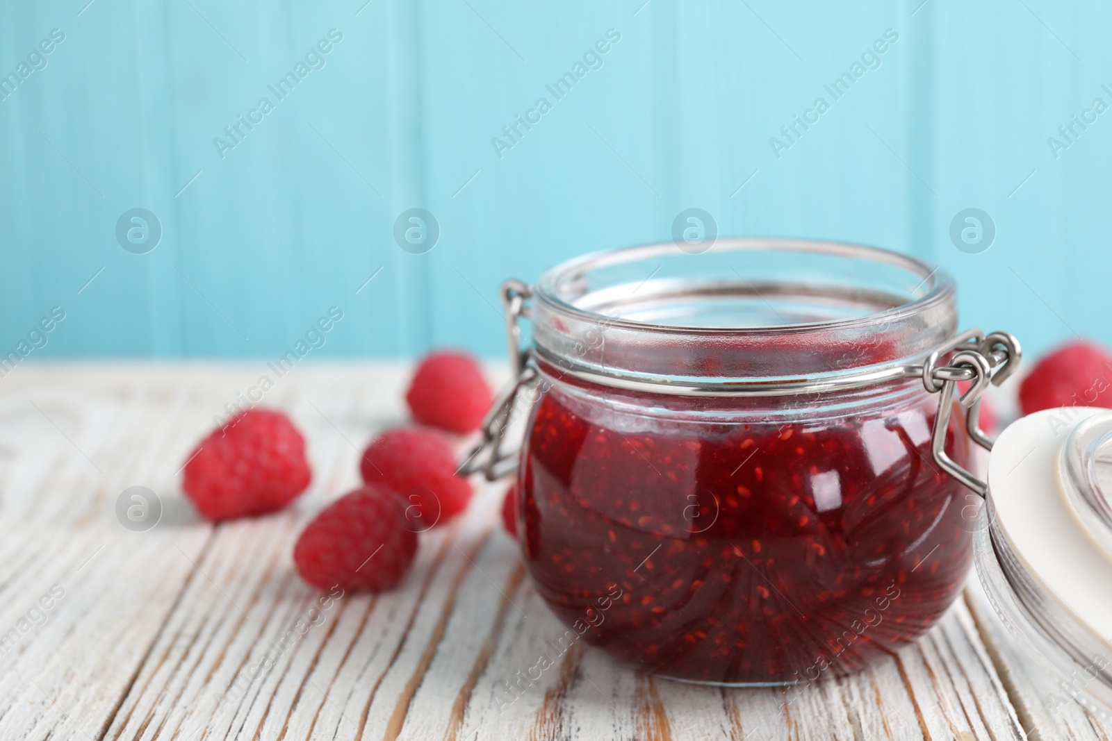 Photo of Delicious jam and fresh raspberries on white wooden table. Space for text