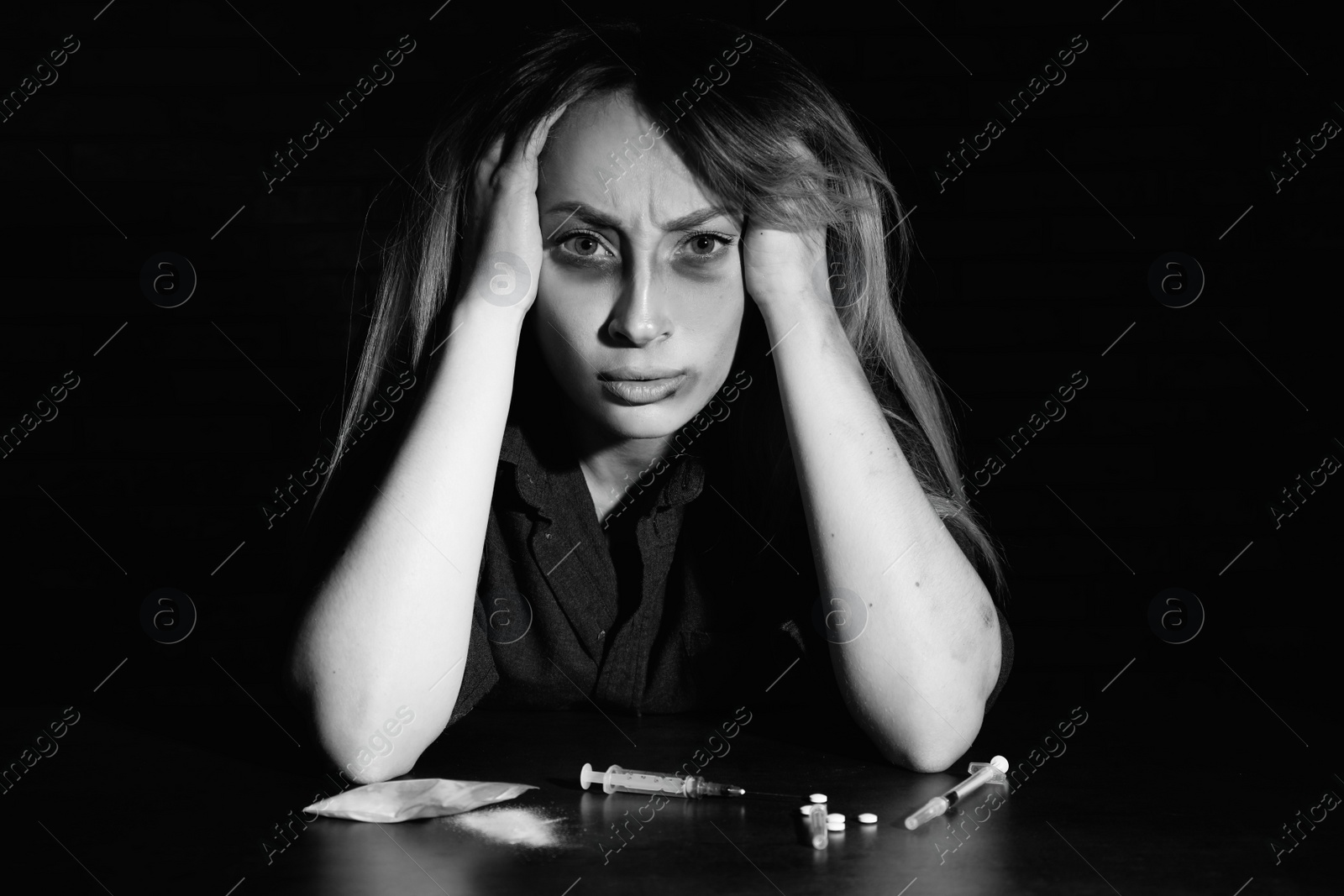 Photo of Addicted woman at table with different drugs, black and white effect