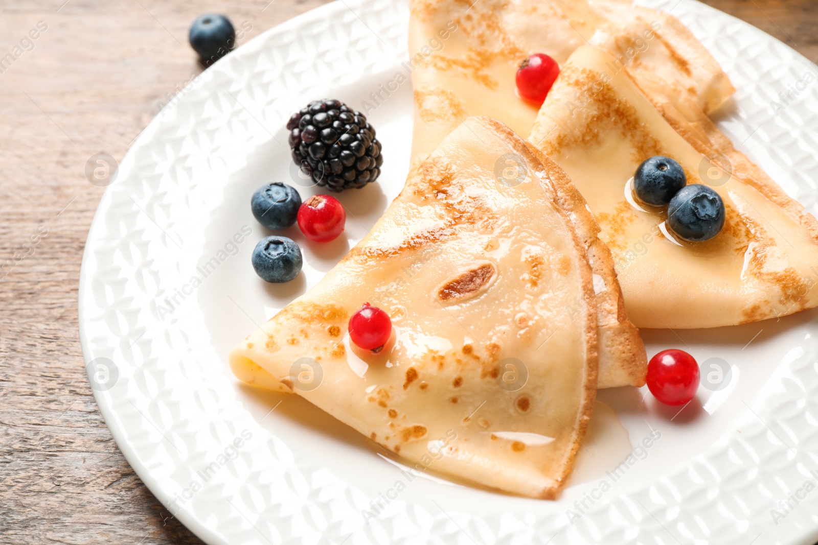 Photo of Delicious thin pancakes with berries on wooden table, closeup