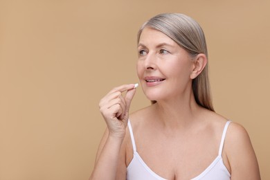 Beautiful woman taking vitamin pill on beige background, space for text